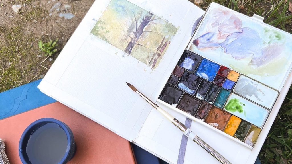 Plein air setup with portable watercolor kit on sketchbooks.