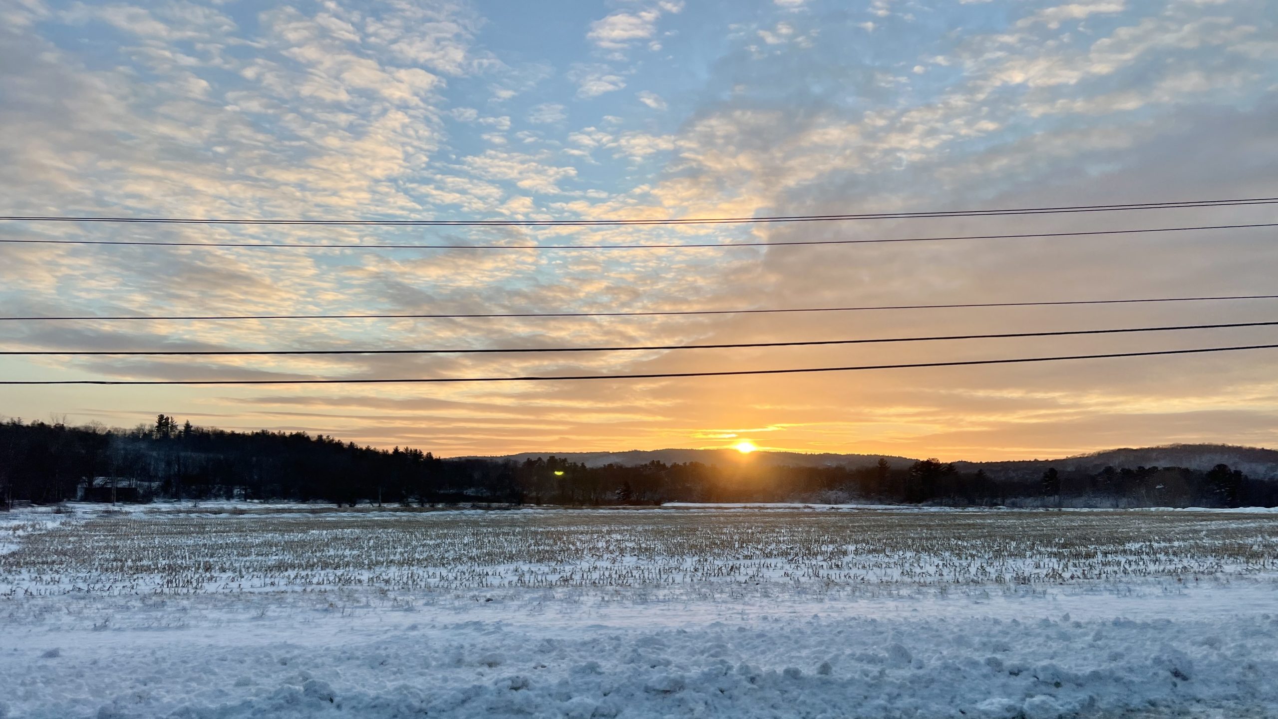 Photograph of a colorful sunset over the low moutnain ridge with a snowy cornfield in the foreground.